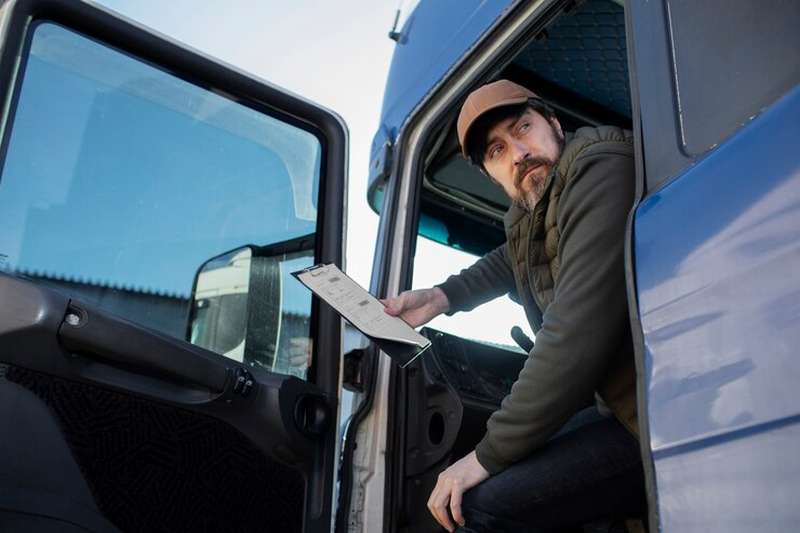 Kierowca ciężarówki w kabinie trzyma dokumenty.
